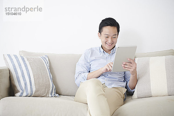 Junger japanischer Mann mit Tablet auf dem Sofa