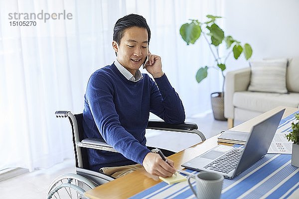 Japanischer junger Mann im Rollstuhl arbeitet von zu Hause aus