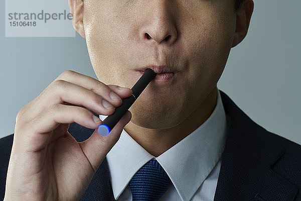 Junger japanischer Mann  der eine elektronische Zigarette raucht