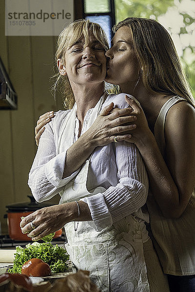 Tochter küsst ihre Mutter in der Küche