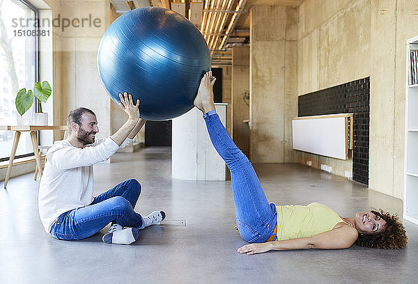 Glücklicher Mann und Frau üben mit dem Fitnessball im modernen Büro