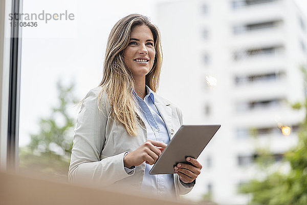 Porträt einer jungen Geschäftsfrau mit Tablett  im Hintergrund Bürogebäude