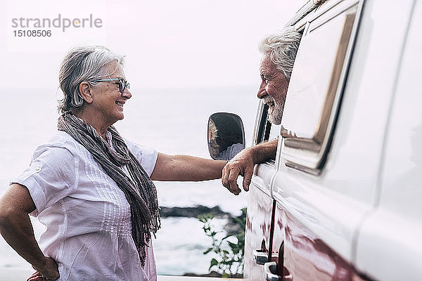 Älteres Ehepaar reist in einem Oldtimer-Van  macht eine Pause am Meer  unterhält