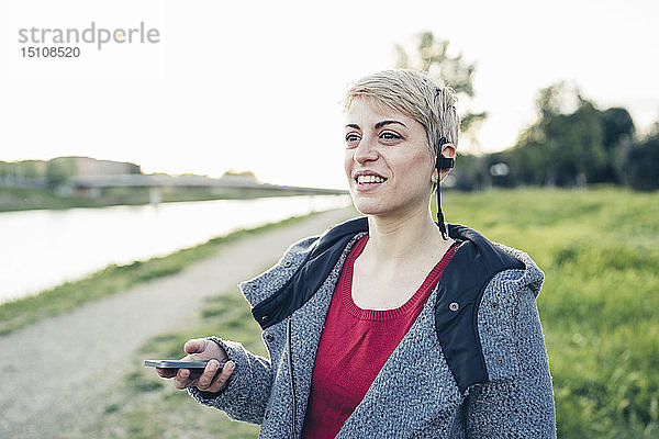 Porträt einer lächelnden Frau  die ein Smartphone und Headset im Freien benutzt