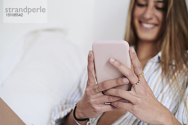 Junge Frau sitzt auf dem Bett und benutzt ein Smartphone