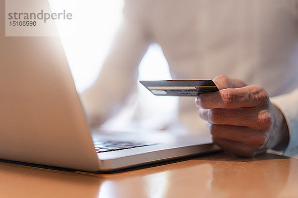 Männerhände  die eine Kreditkarte halten und während einer Online-Zahlung mit einem Laptop  Nahaufnahme