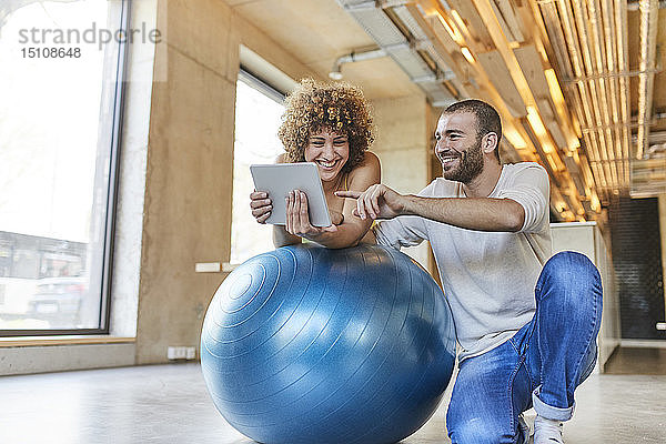 Glücklicher Mann und Frau mit Tablette auf Fitnessball im modernen Büro