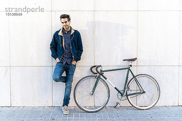 Porträt eines Mannes mit Fahrrad an einer Mauer stehend