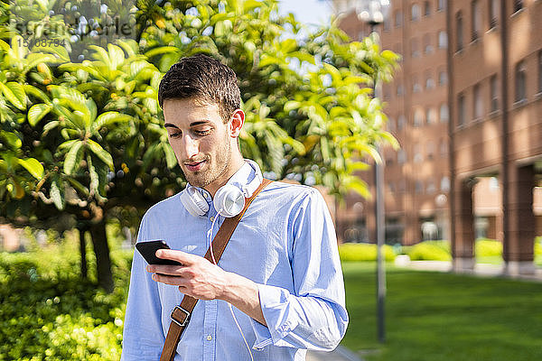 Junger Mann benutzt Smartphone  Kopfhörer um den Hals