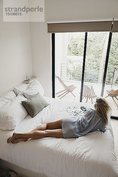 Junge Frau mit Fotos im Bett liegend