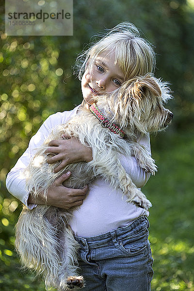 Porträt eines glücklichen kleinen Mädchens mit ihrem Hund im Garten