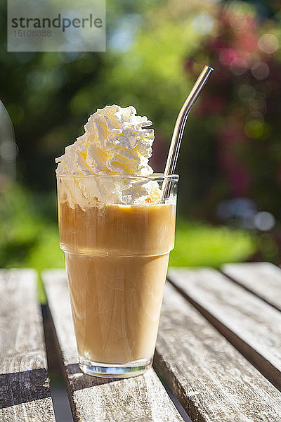 Glas Eiskaffee mit Sahnehaube auf dem Gartentisch