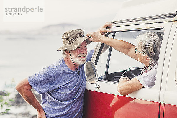 Älteres Ehepaar reist in einem Oldtimer-Van  macht eine Pause am Meer  unterhält