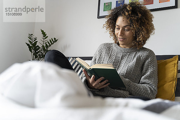 Frau sitzt auf Bett  liest Buch