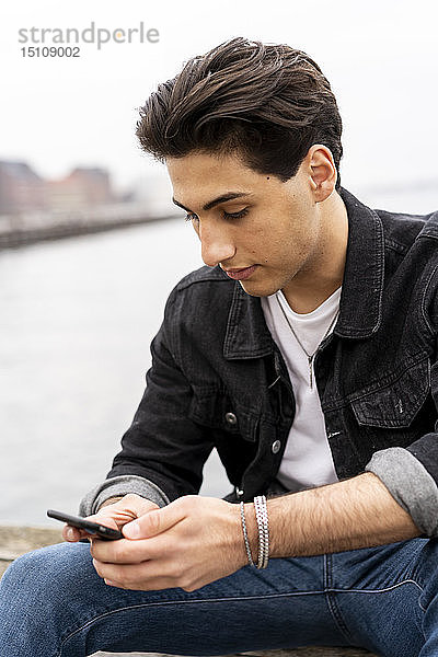Dänemark  Kopenhagen  junger Mann sitzt am Wasser und telefoniert