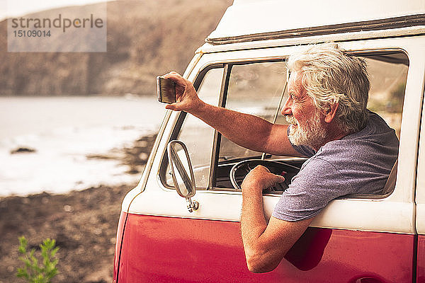 Älterer Mann reist in einem Kleinbus und fotografiert das Meer