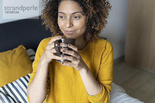 Frau sitzt auf dem Bett  macht eine Pause  trinkt Kaffee