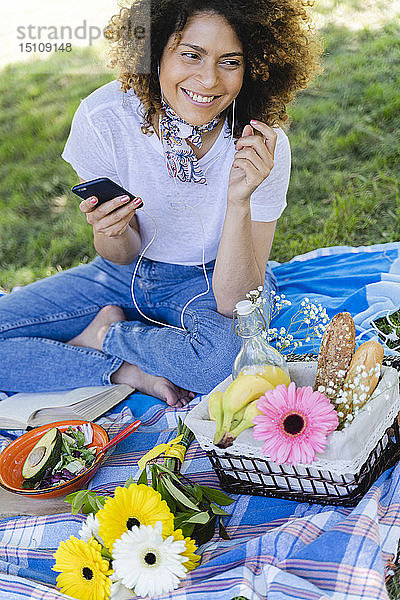 Entspannte Frau mit Handy und Kopfhörern beim Picknick im Park