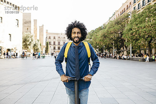 Porträt eines lächelnden Mannes mit Rucksack auf seinem E-Scooter nach der Arbeit  Barcelona  Spanien