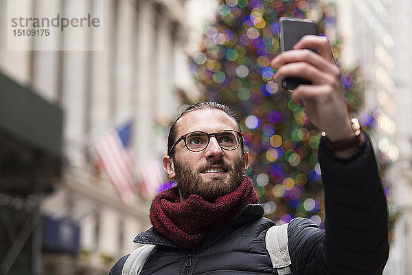 Porträt eines Touristen  der sich mit einem Smartphone vor einem beleuchteten Weihnachtsbaum selbstständig macht  New York City  USA