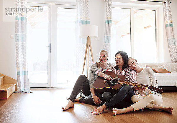 Reife Frau mit zwei Töchtern  die zu Hause auf dem Boden sitzen und Gitarre spielen