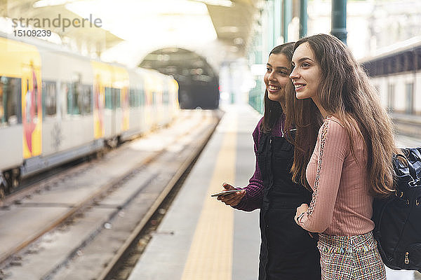 Zwei junge Frauen mit Rucksack und Handy stehen auf einem Bahnsteig und beobachten etwas  Porto  Portugal