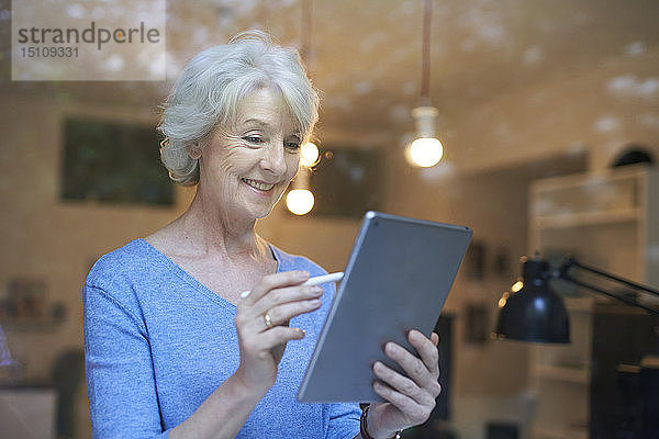 Porträt einer lächelnden reifen Frau hinter einer Fensterscheibe mit digitalem Tablett