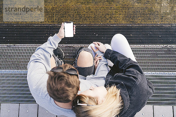 Junges Paar sitzt auf der Treppe und schaut auf ein Smartphone