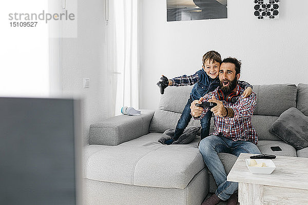 Aufgeregte Vater und Sohn spielen zu Hause Computerspiel