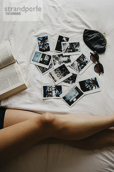Beine einer jungen Frau im Bett mit Buch- und Polaroidbildern