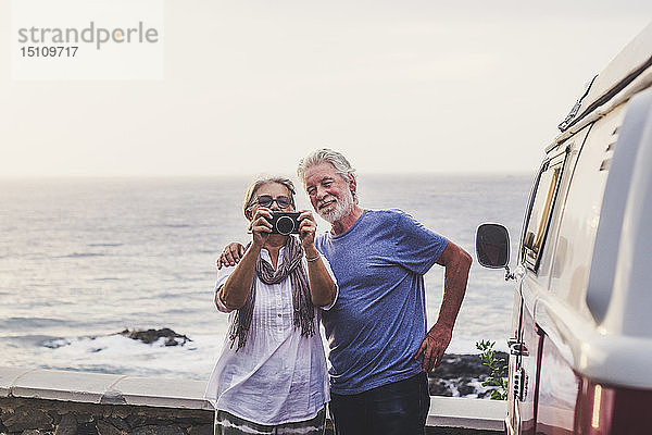 Älteres Ehepaar reist in einem Oldtimer-Van und fotografiert am Meer