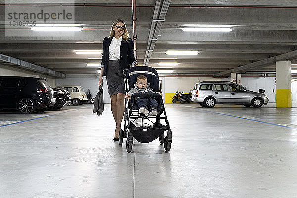 Junge Geschäftsfrau schiebt Kinderwagen mit kleinem Jungen auf dem Parkplatz