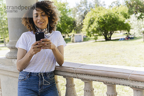 Lächelnde Frau mit Handy und Kopfhörern im Park