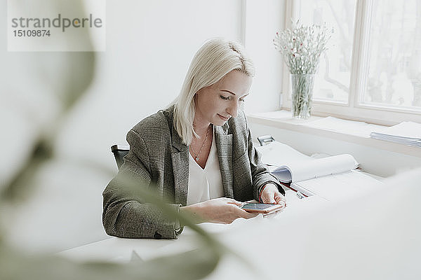 Junge Frau benutzt Handy am Schreibtisch im Büro