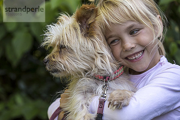 Porträt eines glücklichen kleinen Mädchens  das seinen Hund kuschelt