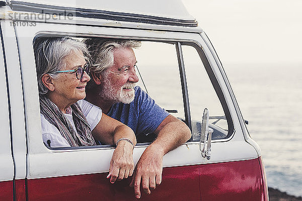 Älteres Ehepaar reist in einem Oldtimer-Van und schaut auf das Meer