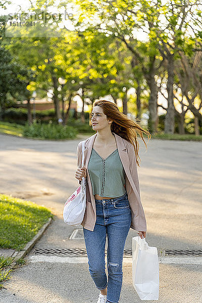 Junge rothaarige Frau mit Einkaufstaschen in einem Park