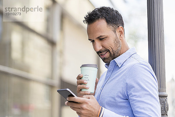 Geschäftsmann mit Kaffee zum Mitnehmen und Mobiltelefon in der Stadt