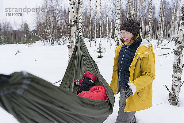 Finnland  Kuopio  Mutter mit Tochter in Hängematte in Winterlandschaft