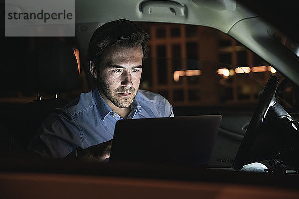 Junger Mann benutzt Laptop nachts im Auto