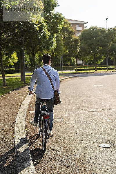 Rückansicht eines jungen Mannes  der auf der Straße Fahrrad fährt