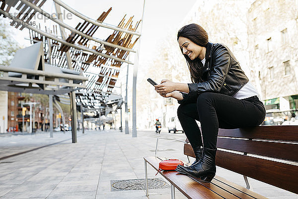 Junge Frau sitzt auf einer Bank und benutzt ein Smartphone