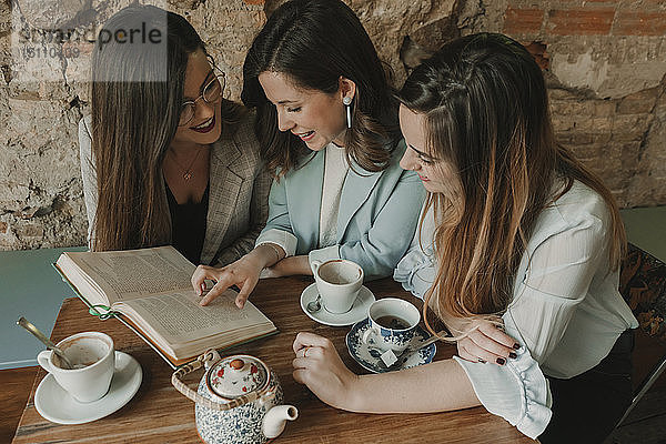 Drei junge Frauen lesen ein Buch in einem Cafe