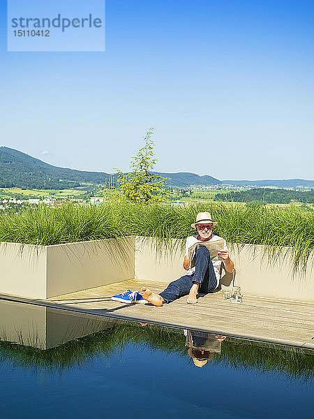 Älterer Mann liest Zeitung im Schwimmbad