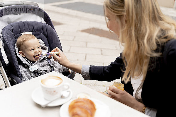 Mutter füttert lachendes Baby Junge im Kinderwagen
