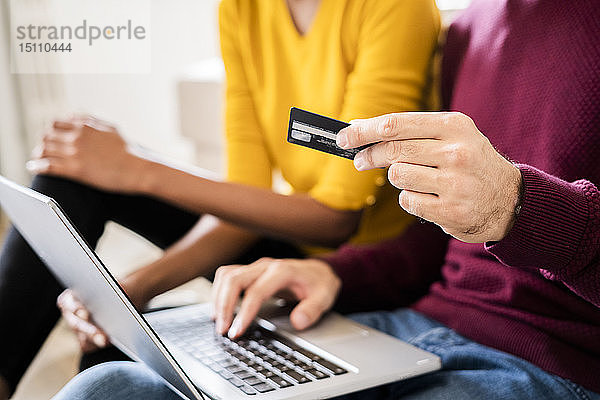 Nahaufnahme eines Paares beim Online-Einkauf zu Hause mit Laptop und Kreditkarte