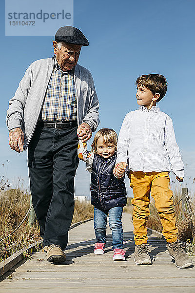 Großvater schlendert mit seinen Enkelkindern Hand in Hand auf der Promenade