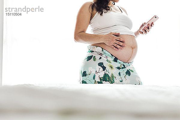 Mittelsektion einer schwangeren Frau mit Mobiltelefon