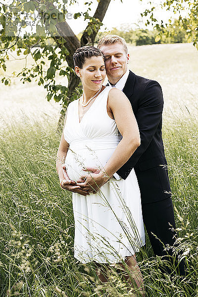 Schwangere Braut mit ihrem Ehemann mit Babybauch auf einer Wiese