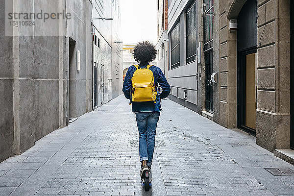 Rückenansicht eines jungen Mannes mit gelbem Rucksack auf einem E-Scooter in der Stadt  Barcelona  Spanien